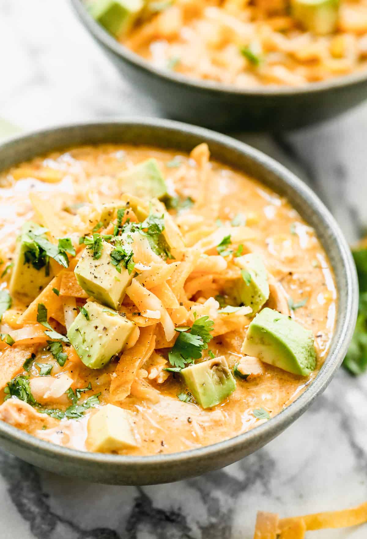 A close-up picture of a bowl of the best White Chicken Chili with cheese, avocados, tortilla chips, and cilantro on top. 