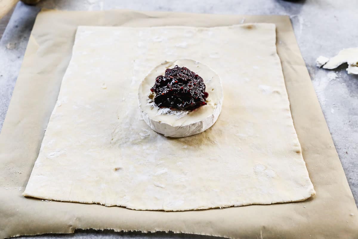 A wheel of brie with jam on it in the center of a puff pastry.