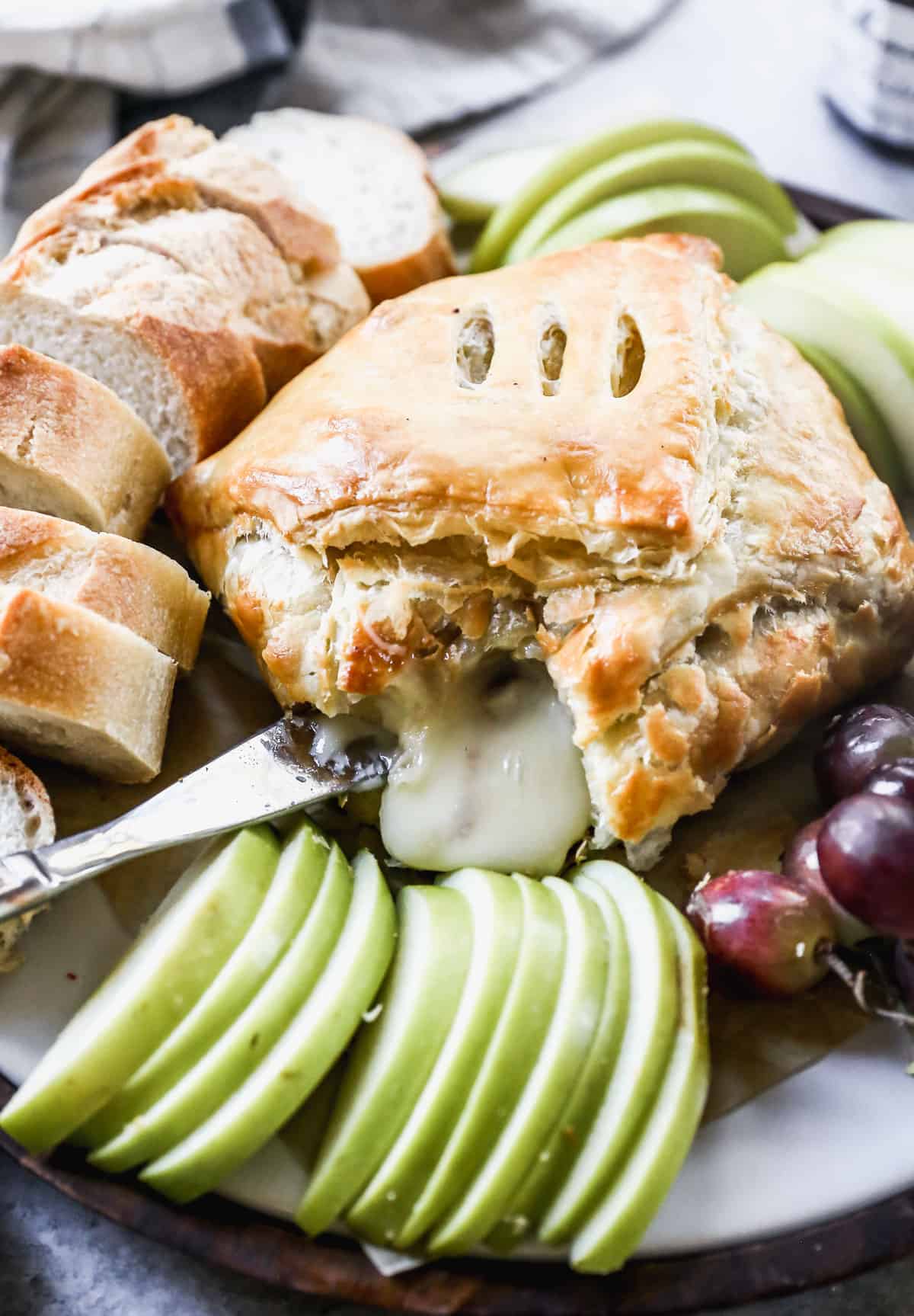 A close-up image of Baked Brie wrapped in puff pastry with some of the melted cheese coming out.