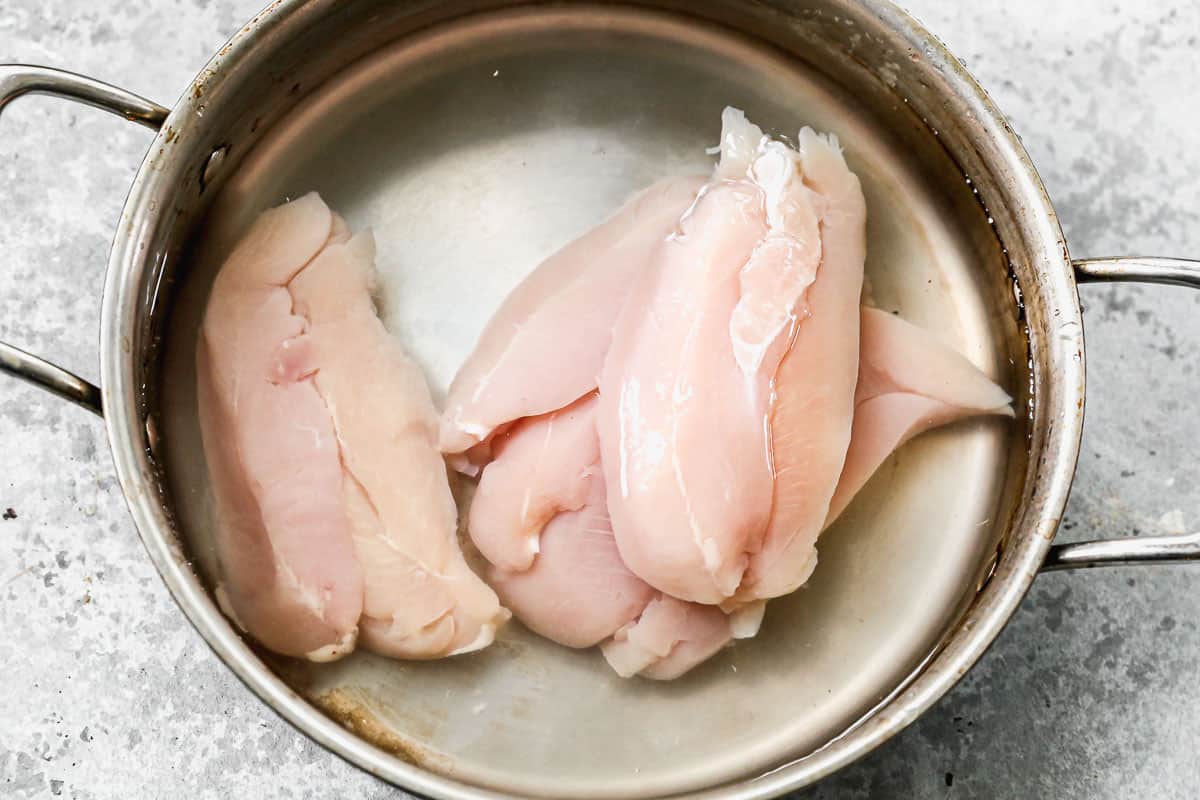 Dada ayam mentah dalam panci berisi air, akan direbus untuk Chicken Pot Pie.