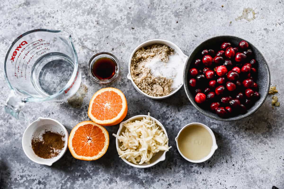 All of the ingredients needed for Cranberry Sauce: fresh cranberries, sugars, apple, oranges, vanilla, apple cider vinegar, and spices.