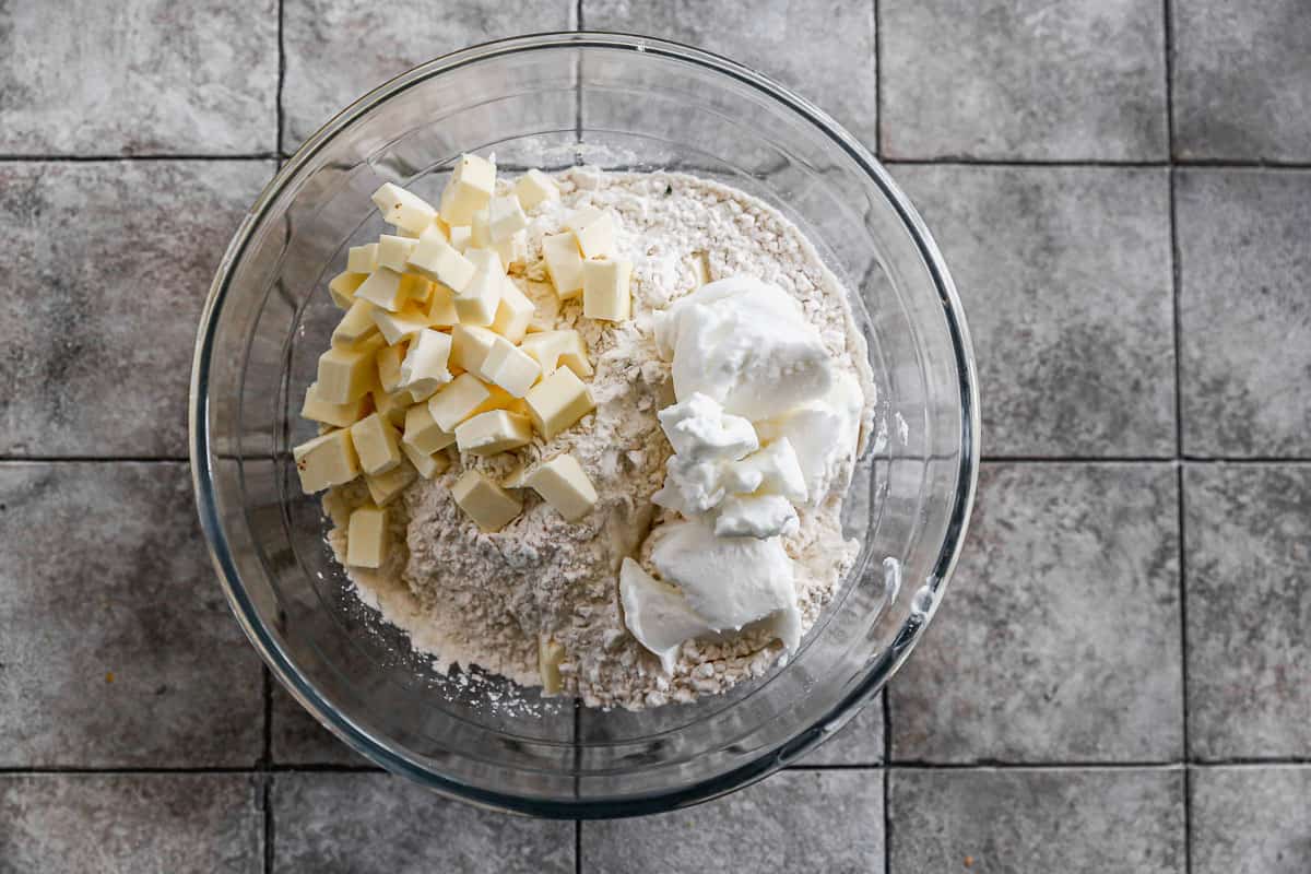A glass mixing bowl with flour, salt, cold shortening, and butter. 