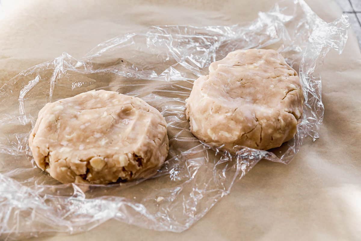 Two discs made out of pie dough on top of plastic wrap and parchment paper.