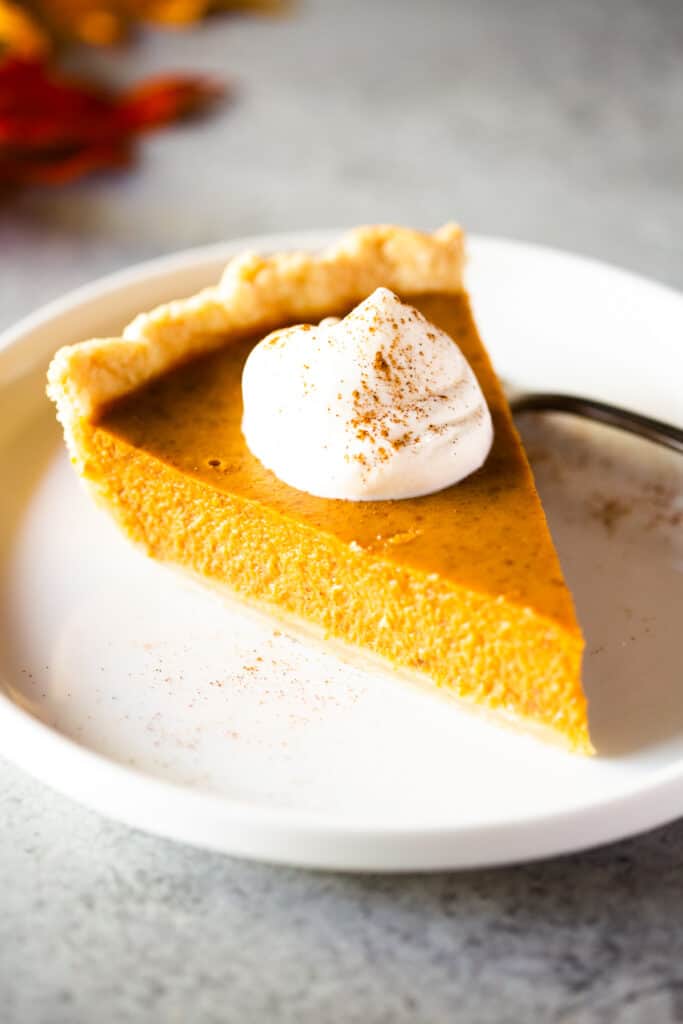 A slice of homemade pumpkin pie with whipped cream.