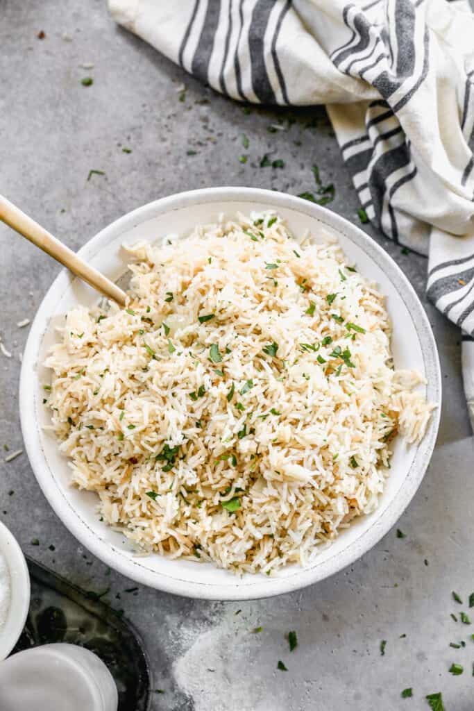 A serving bowl filled with easy Rice Pilaf, and sprinkled with fresh parsley.