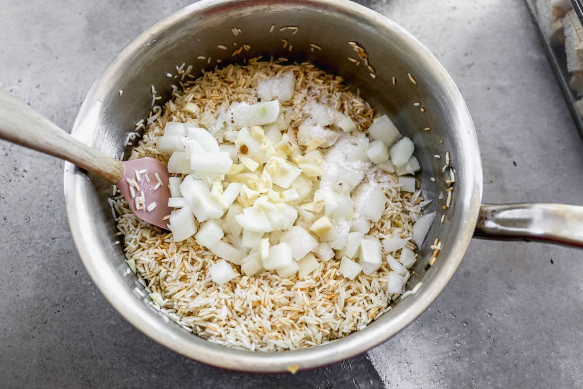 Nasi panggang dengan bawang merah, bawang putih, dan garam dan merica ditambahkan ke dalam panci.