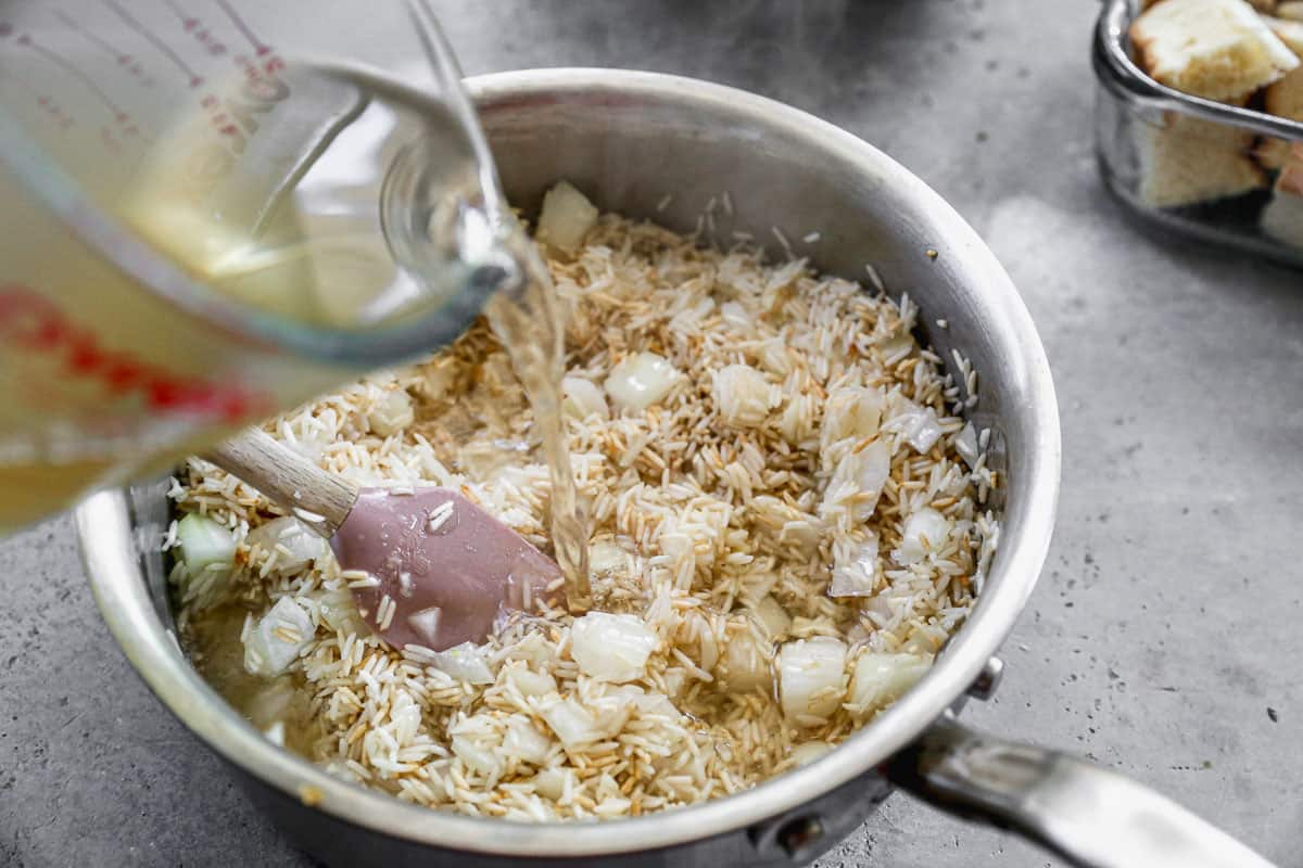 Chicken broth being poured on top of toasted rice with onion and garlic to make Rice Pilaf. 