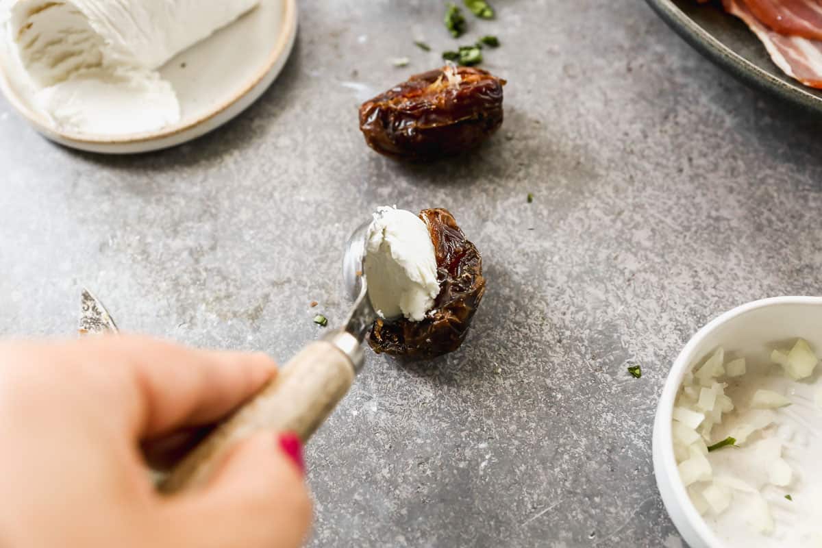 A spoonful of goat cheese being stuffed into a date to make bacon wrapped dates.
