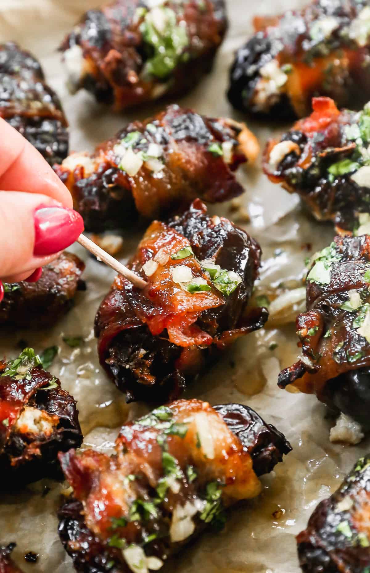 A close up image of bacon wrapped dates with someone about to pick one up with a toothpick.