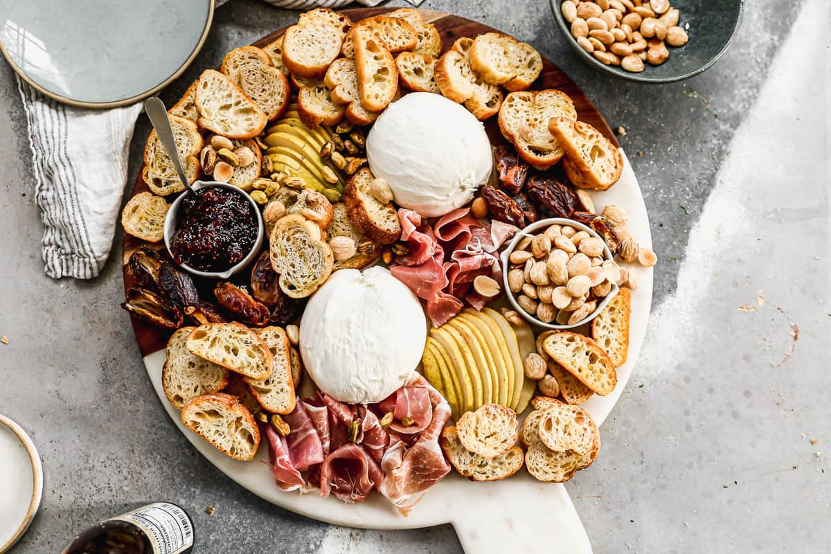Burrata surrounded by pear, prosciutto, dates, jam, toasts, and nuts to make the best burrata appetizer.
