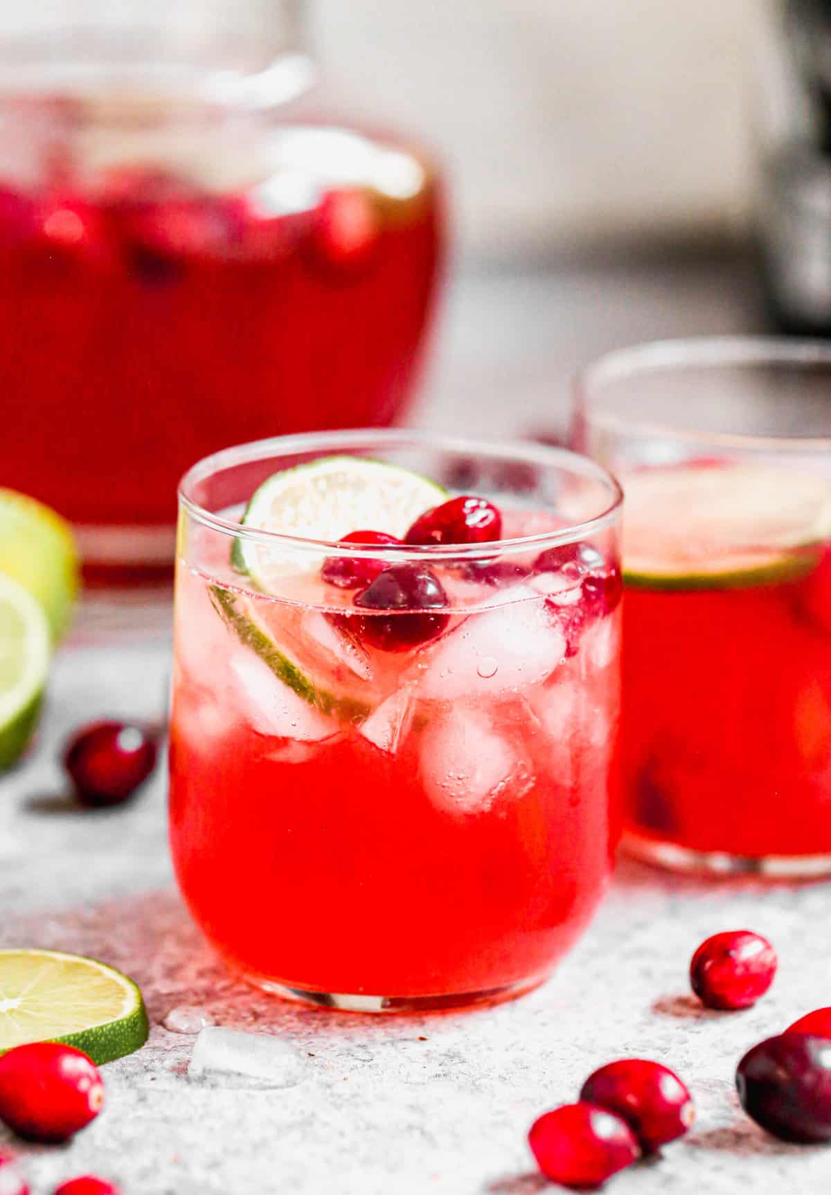 A small glass filled with easy Christmas Punch and topped with cranberries and a lime.