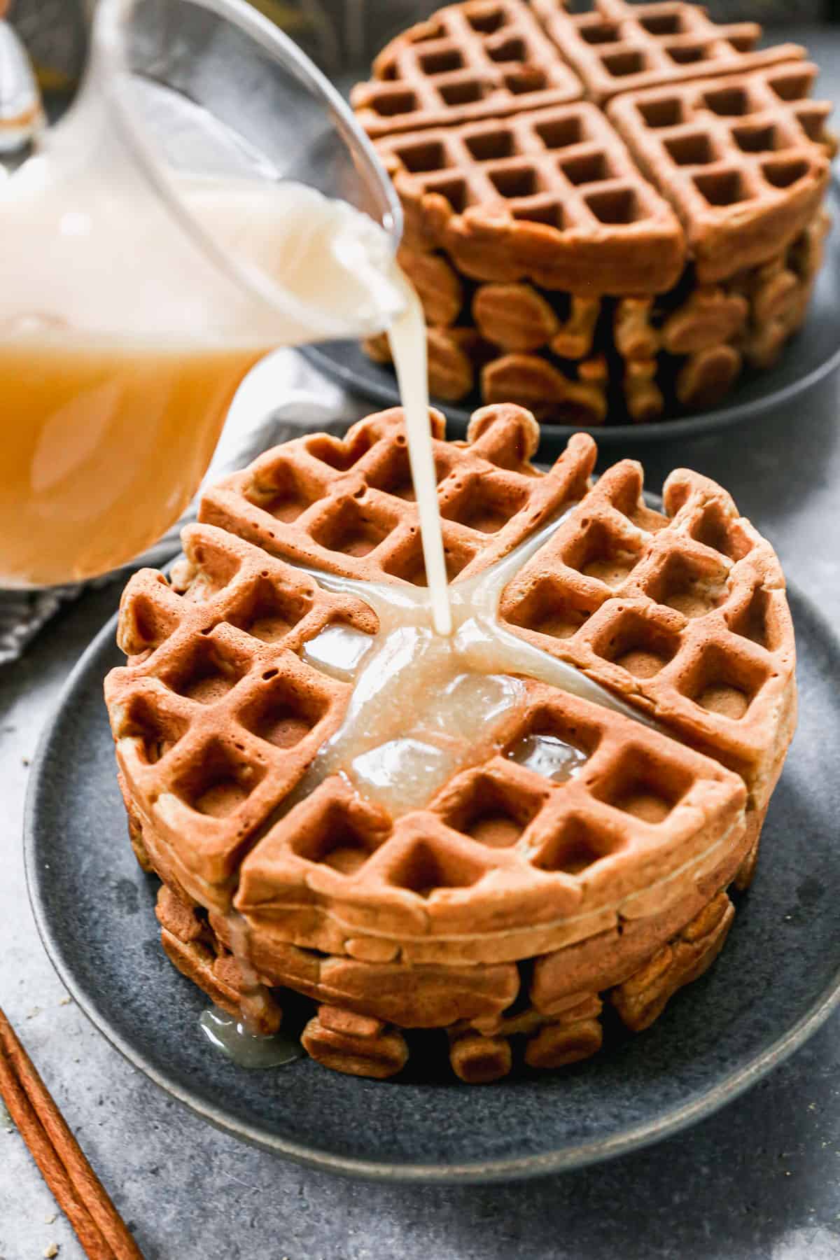 A stack of three Gingerbread Waffles with vanilla syrup being poured on top.