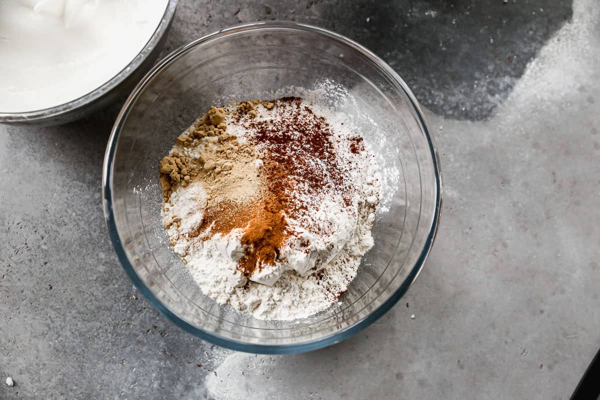 A glass mixing bowl with flour, sugar, baking powder, baking soda, salt, and spices to make easy Gingerbread Waffles.