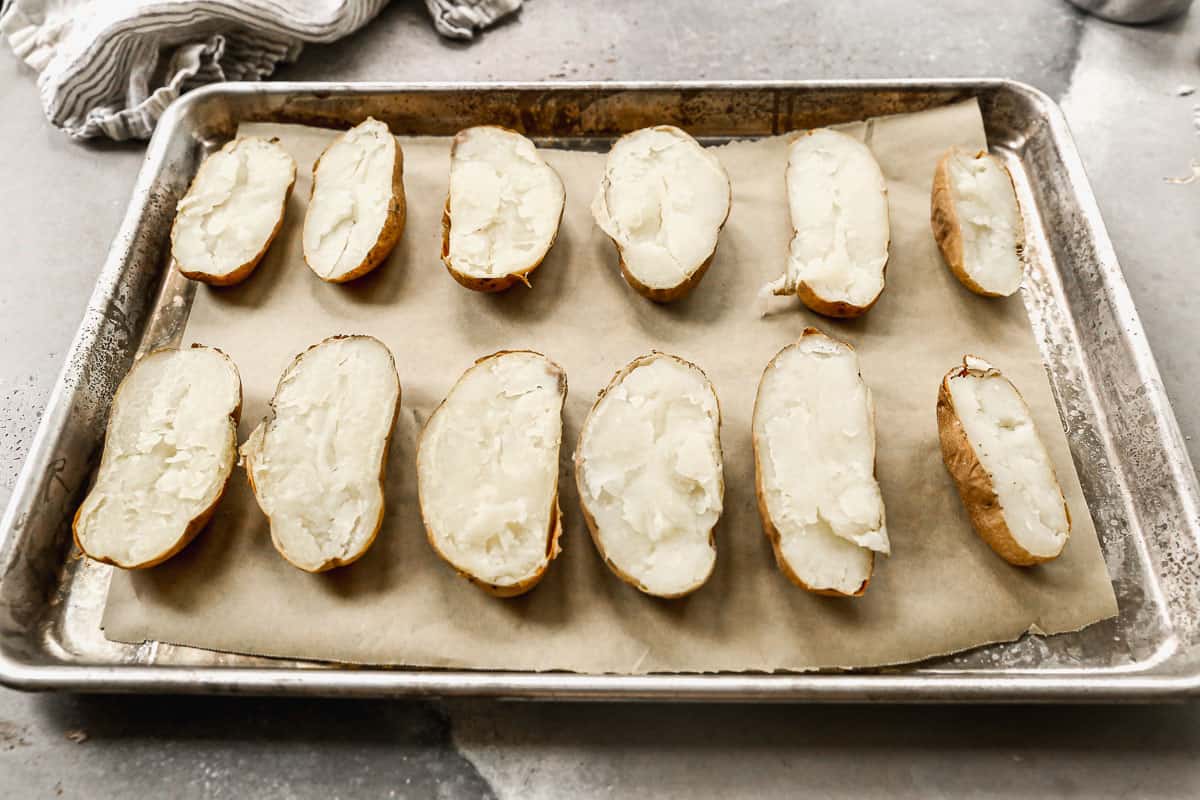 A baking sheet with parchment paper and cooked baked potatoes sliced in half.