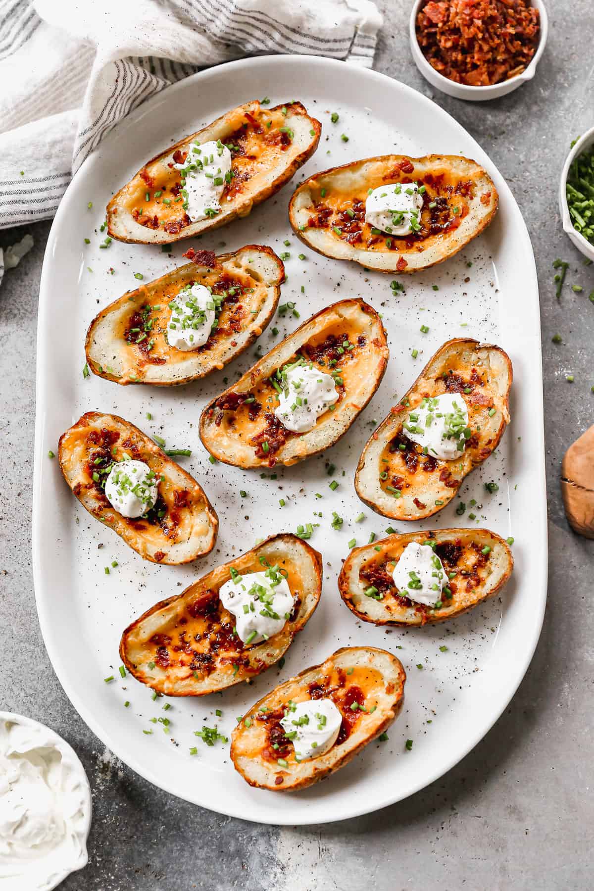 A white platter filled with loaded potato skins and topped with sour cream and chives, ready to serve.