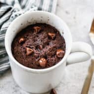 An easy chocolate mug cake in a white mug, topped with chocolate chips.