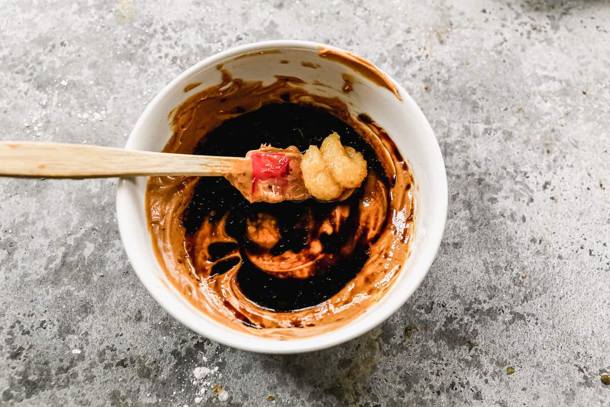 Peanut butter, honey, ginger, soy sauce, vinegar, sesame oil, olive oil, and sriracha in a bowl with a rubber spatula.