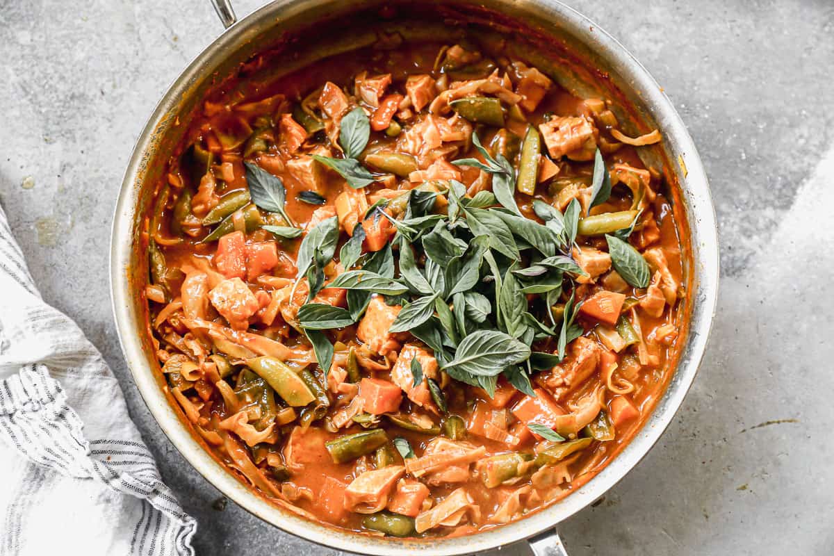 Easy red curry in a large pan topped with Thai basil leaves, ready to serve.