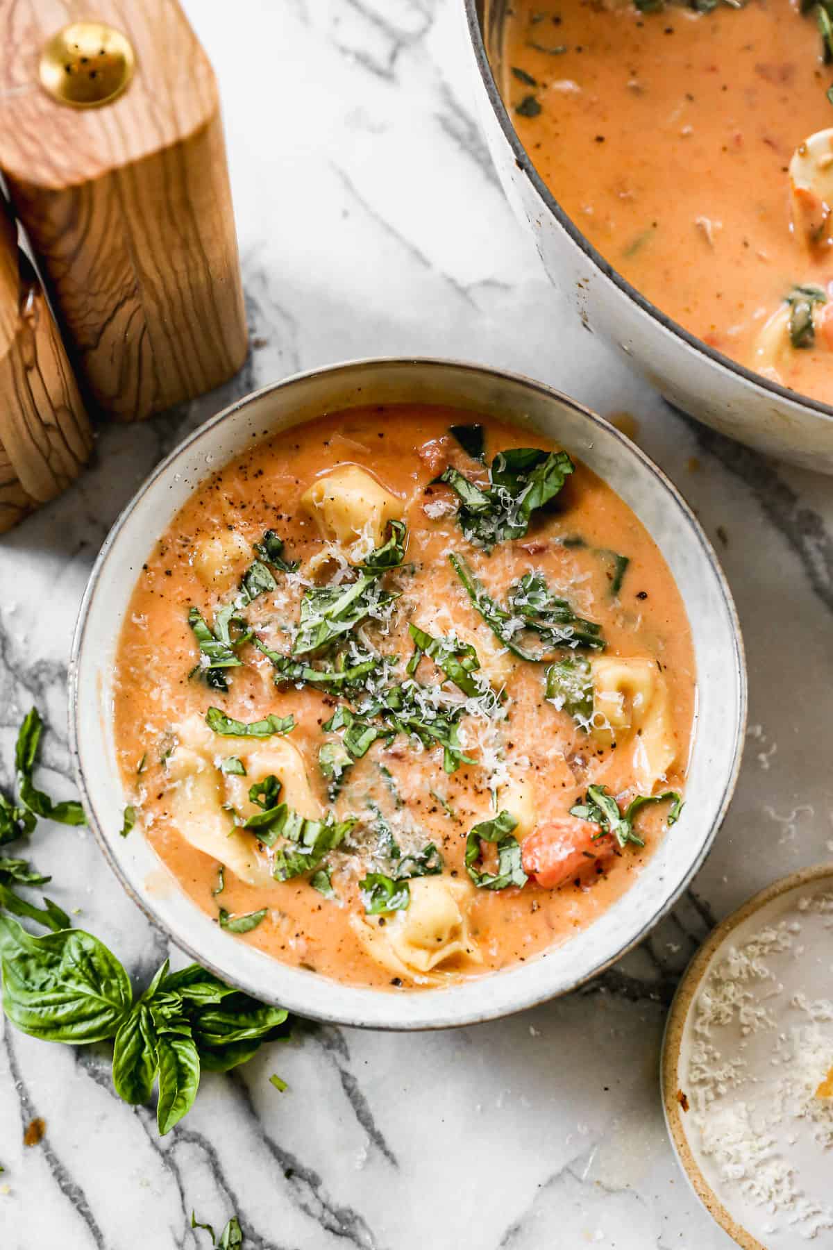 A hot bowl of creamy Spinach Tortellini Soup topped with fresh basil and parmesan cheese.