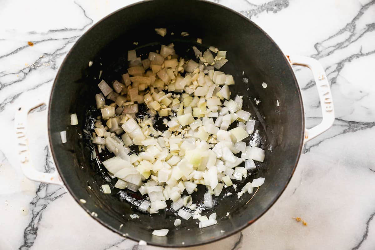A dutch oven pot with diced onion and garlic in butter and oil.