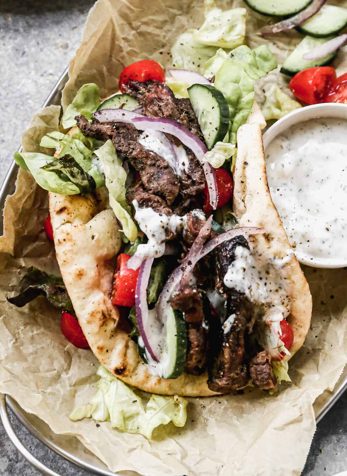 A close up image of a beef gyro with homemade tzatziki sauce and vegetables on top.