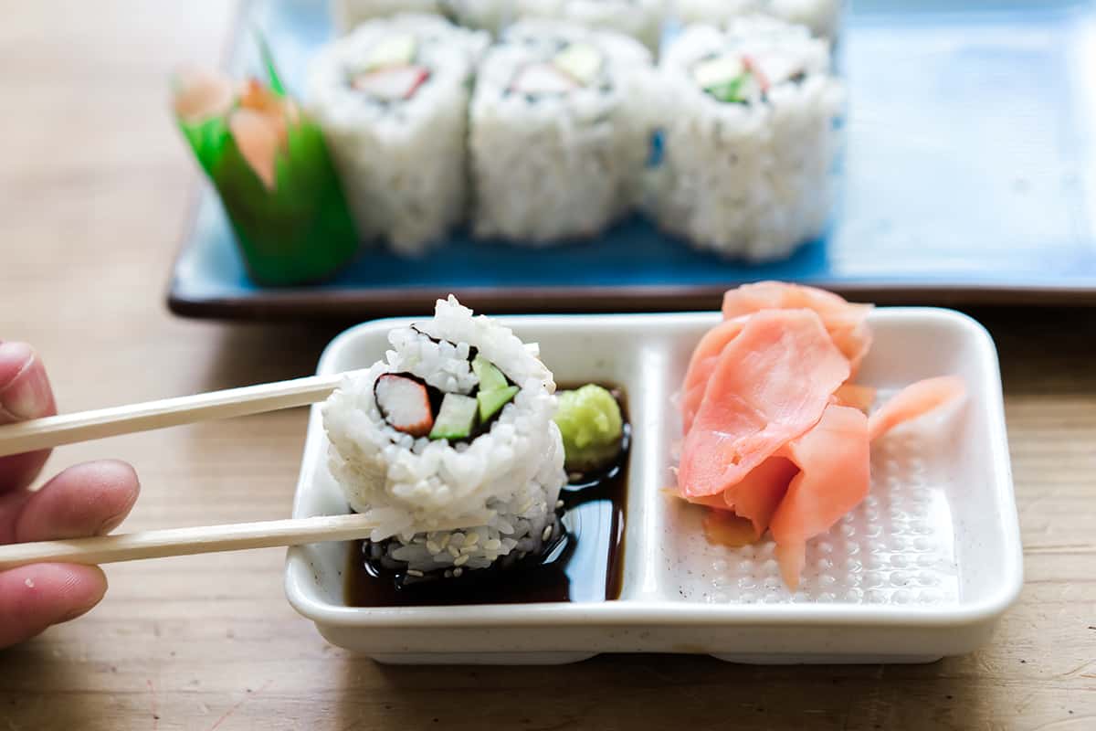 A California Roll being held by chopsticks and dipped in wasabi. 