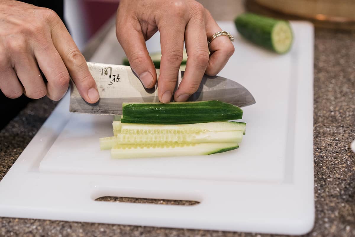 A cucumber being sliced into long chunks for an easy California roll recipe with a Japanese knife.