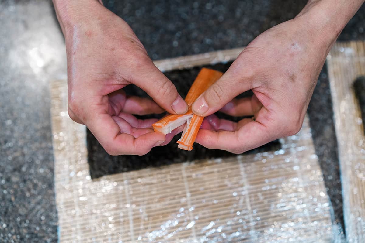 An imitation crab stick being gently pulled apart in half.