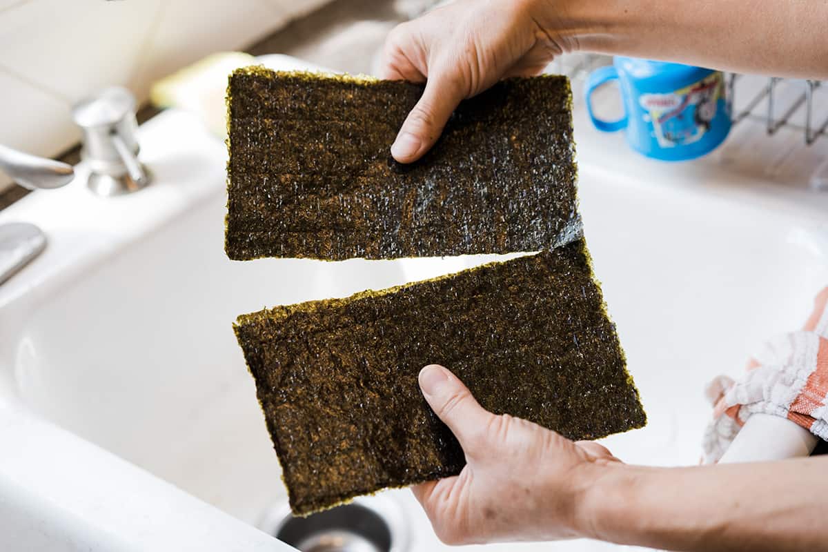 A pile of three Nori seaweed sheets being broken apart in half for a California Roll recipe. 
