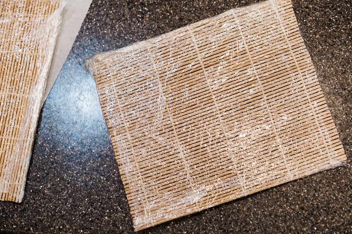 A bamboo sushi mat wrapped in plastic wrap.