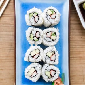 A homemade California Roll served in a group of 8 on a rectangle blue serving plate.