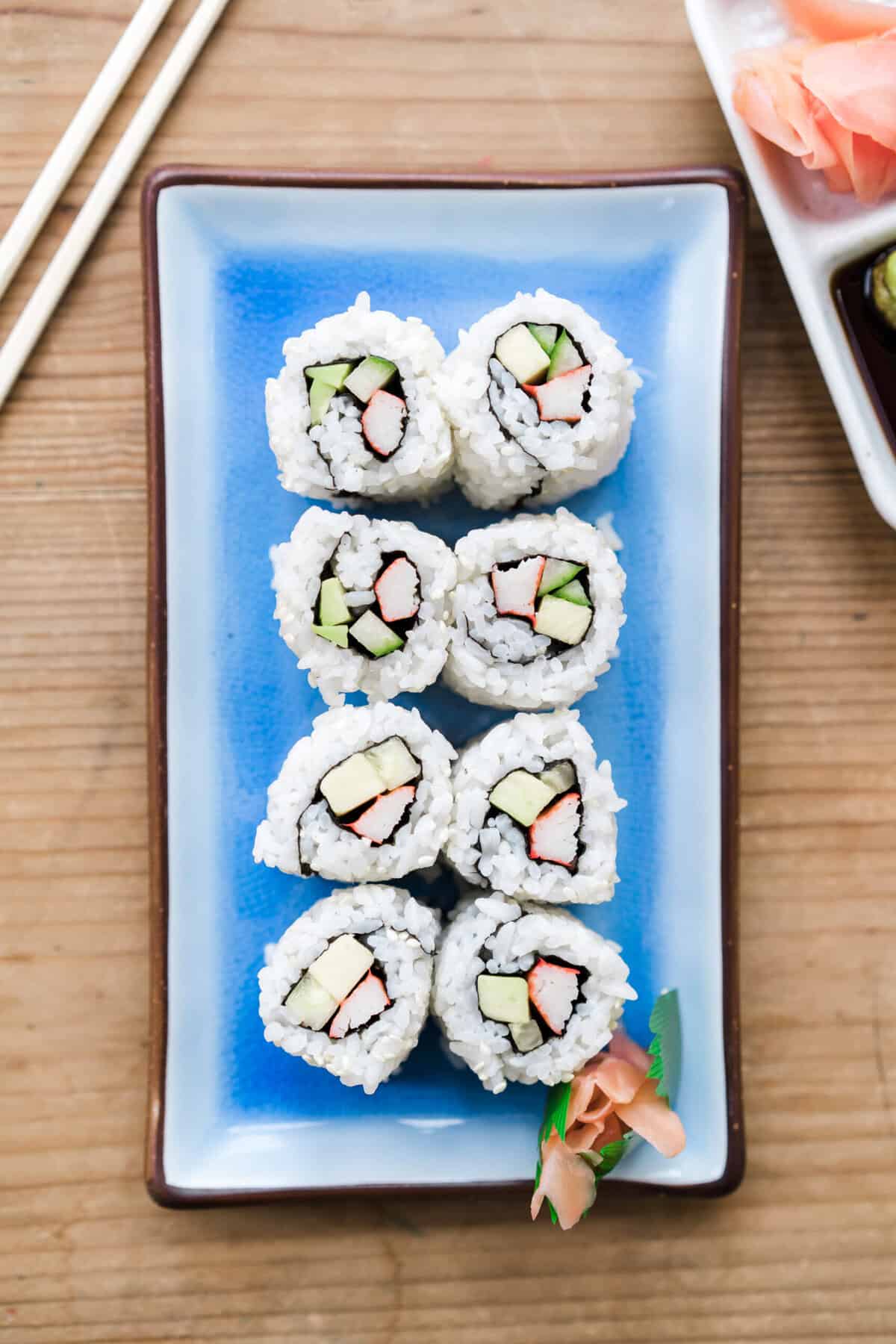 A homemade California Roll served in a group of 8 on a rectangle blue serving plate. 