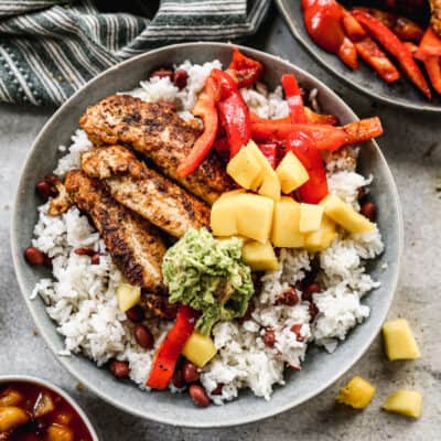 A jerk chicken bowl recipe topped with red bell peppers, fresh mango, and mashed avocado.