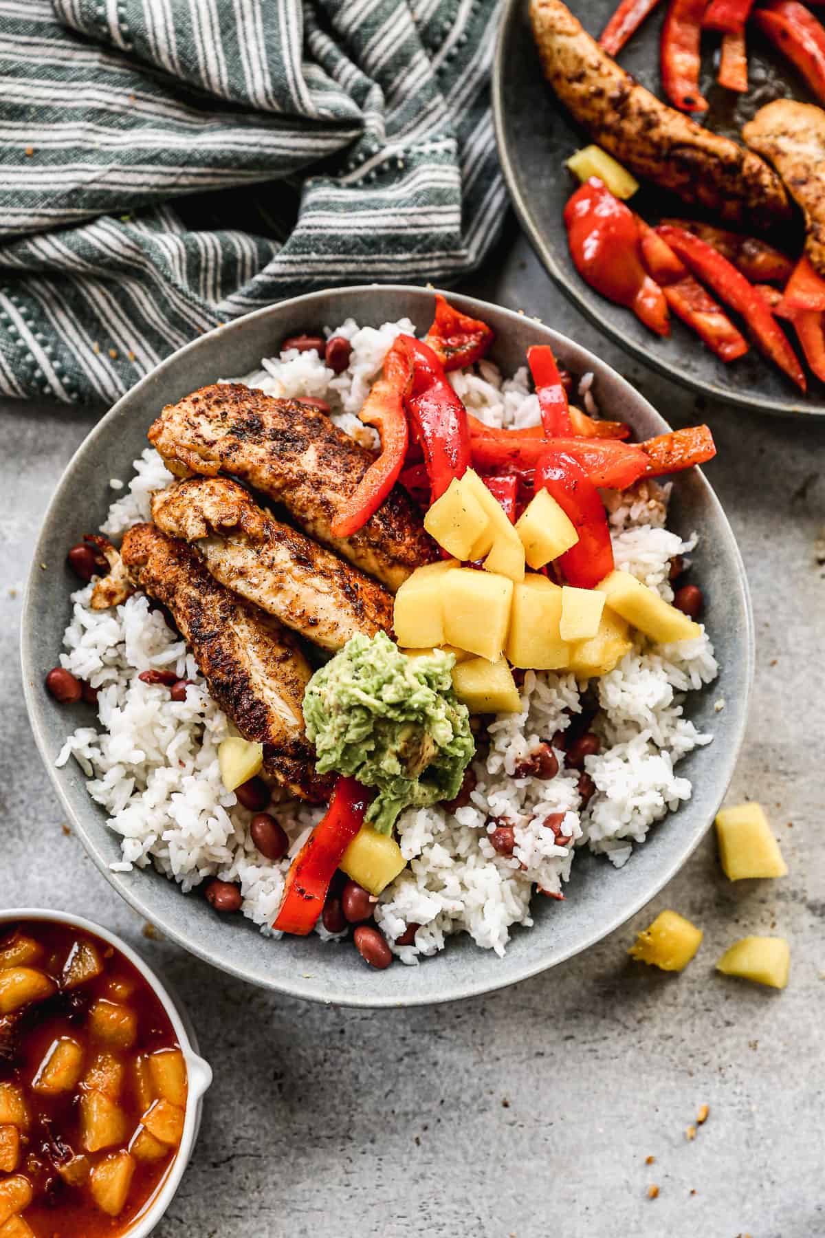 An easy Jerk Chicken Bowl recipe with rice and beans, topped with jerk chicken, red bell pepper, mashed avocado, and fresh mango. 