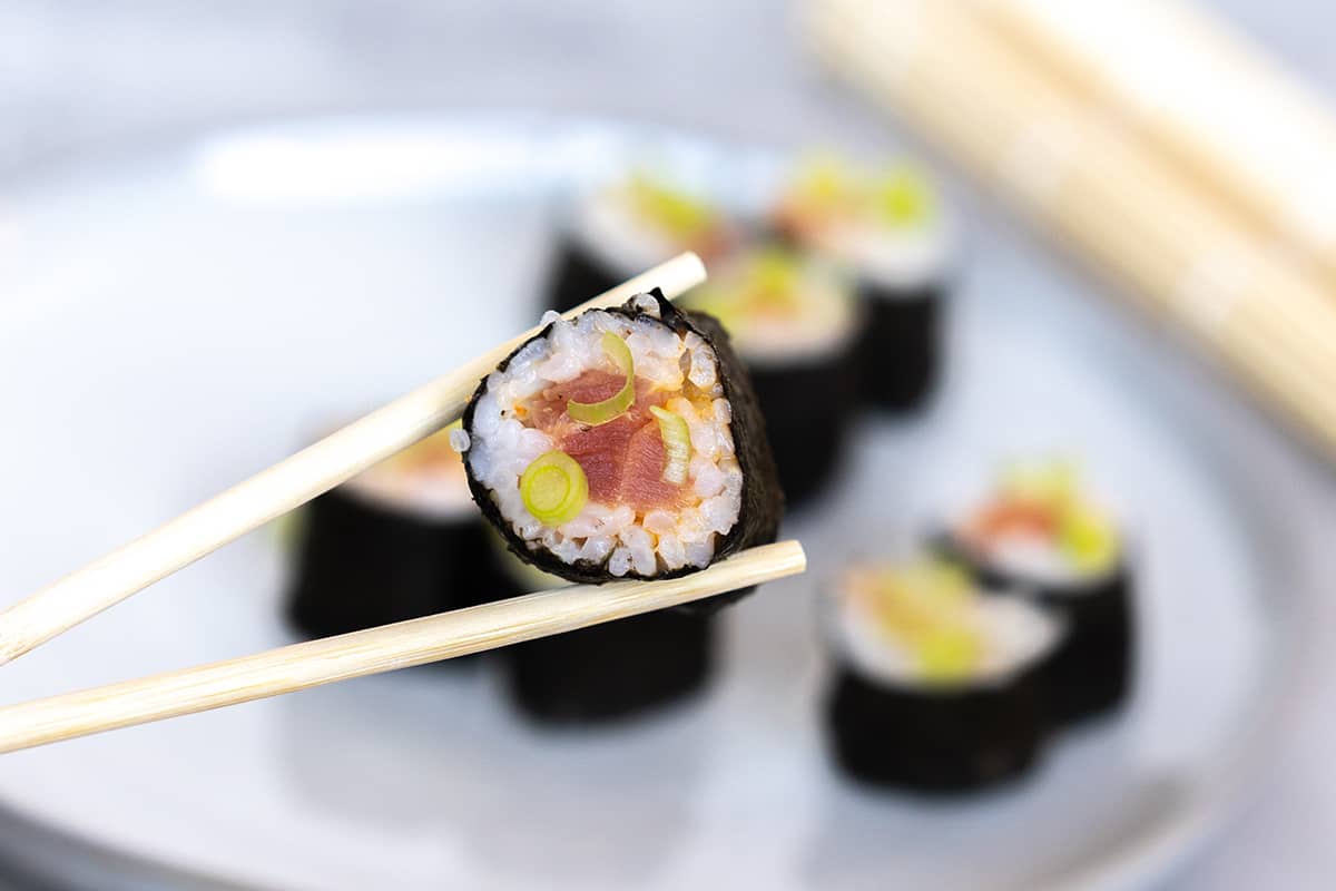 A piece of a Spicy Tuna roll being lifted up with chopsticks. 