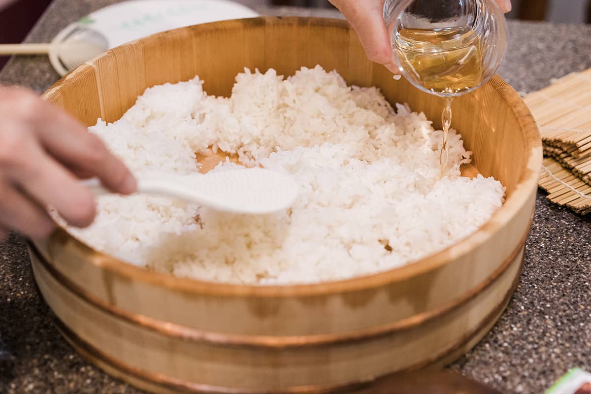 Bumbu nasi sushi dituangkan di atas nasi bulir pendek Jepang untuk menyiapkan sushi.