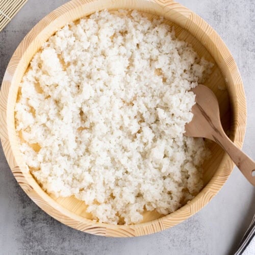 The best Sushi Rice recipe in a wooden bowl with a wooden rice paddle, ready to be used in sushi rolls or bowls.