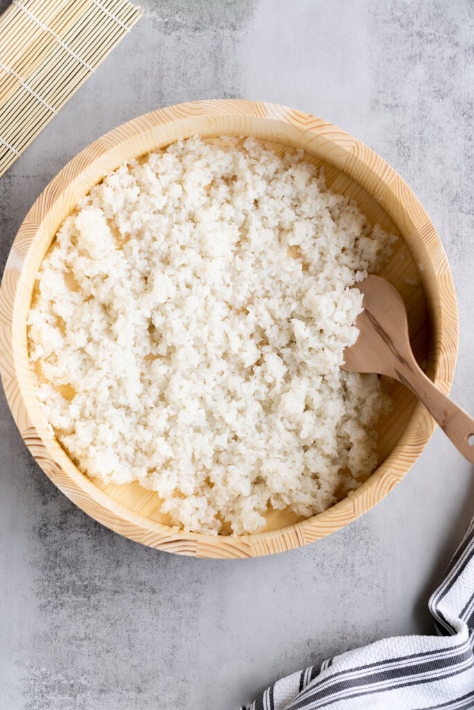 The best Sushi Rice recipe in a wooden bowl with a wooden rice paddle, ready to be used in sushi rolls or bowls.