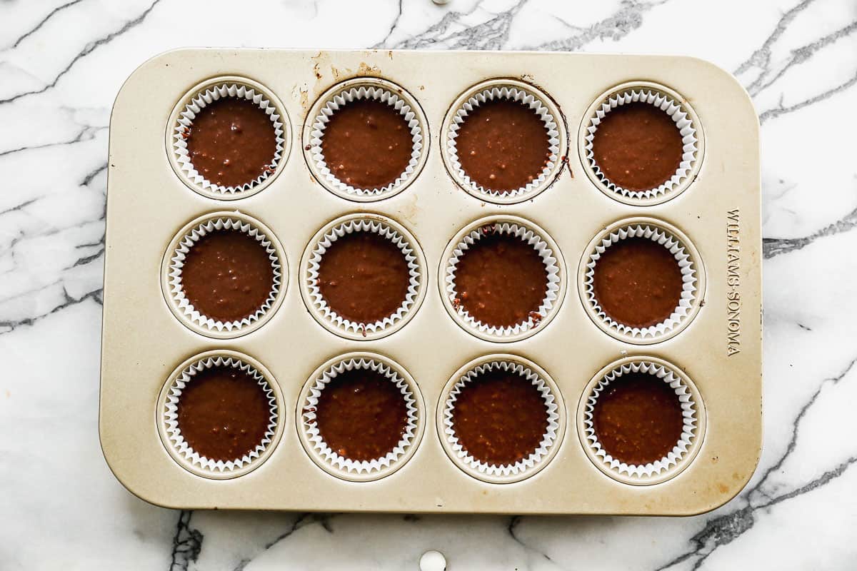 A standard muffin pan with liners, each filled ½ full with chocolate cupcake batter.