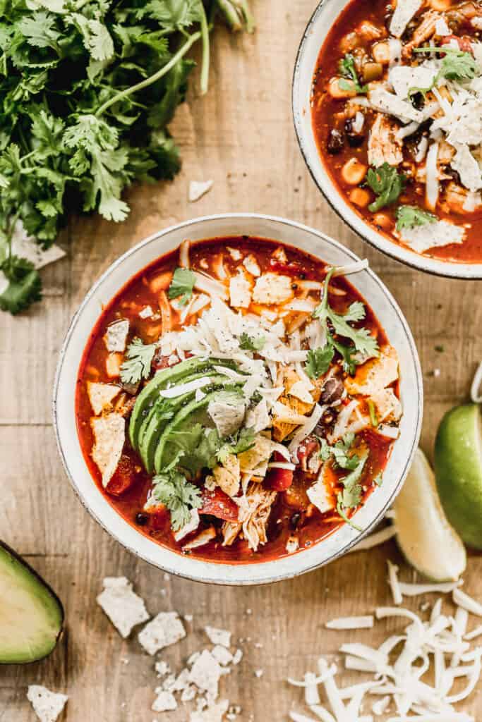 A bowl of homemade Chicken Tortilla Soup with crumbled tortilla soup, cheese, and sliced avocado.