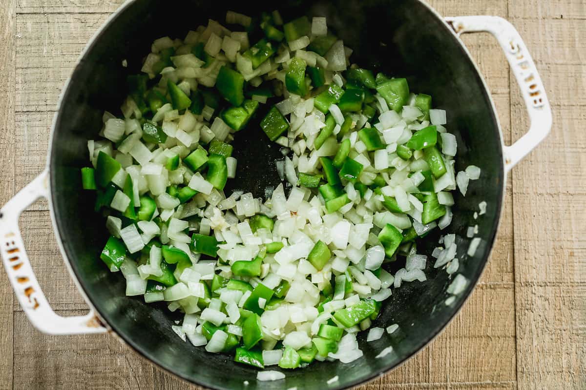 Chopped green bell pepper, onion, and garlic being sautéed in a large pot. 