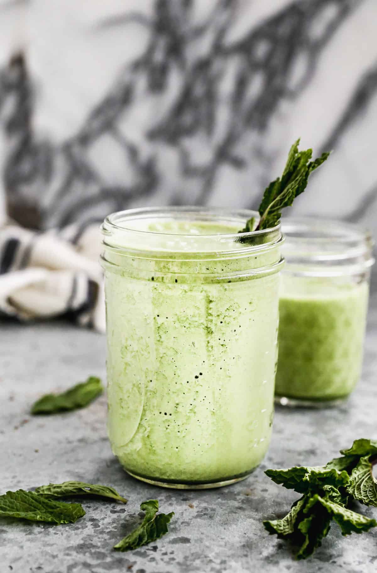 A mason jar filled with a delicious homemade Green Smoothie with a piece of kale sticking out.