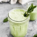 A healthy green smoothie in a mason jar with a piece of kale sticking out.