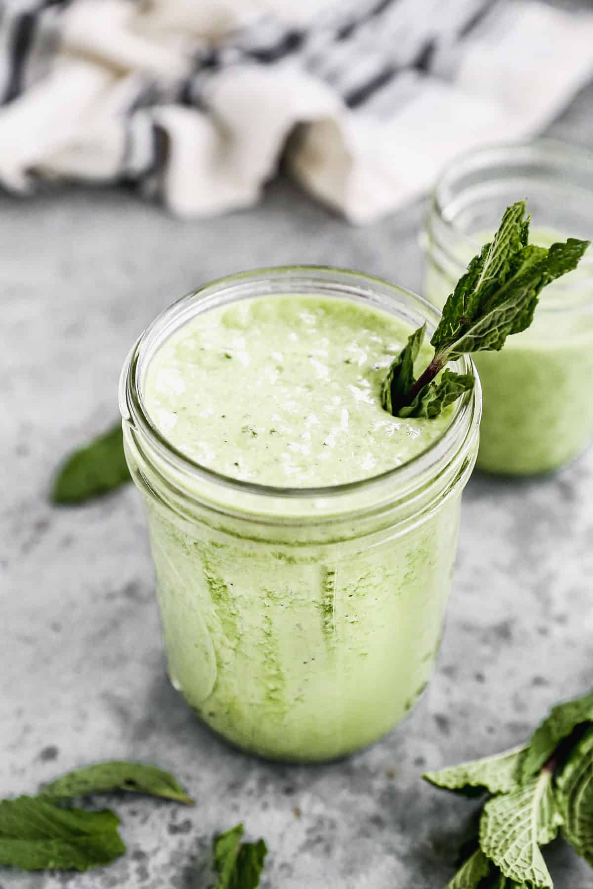 A close up picture of a Green Smoothie in a mason jar with a piece of kale sticking out. 