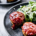 Two mini meatloaf with sauce on a plate with a green salad, ready to be enjoyed!