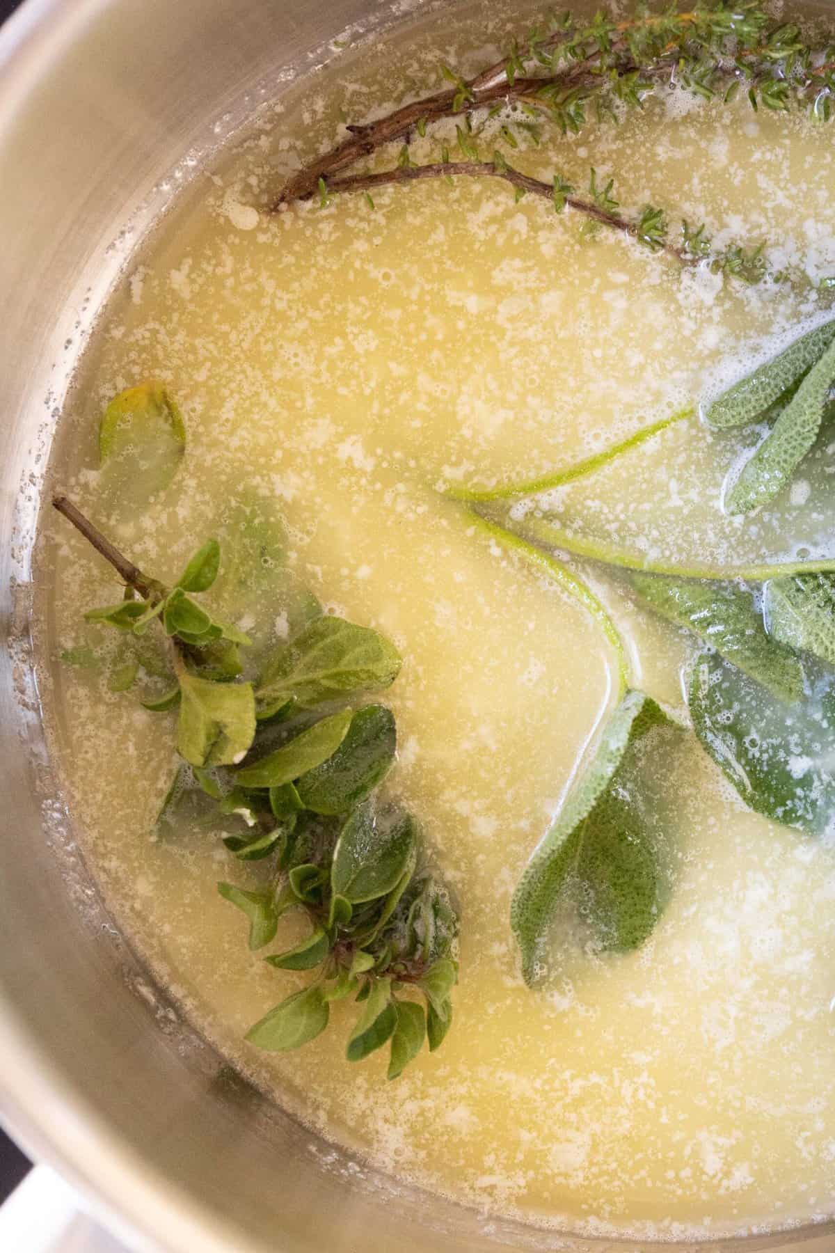 A close-up image of a pot with melted butter and strands of herbs. 