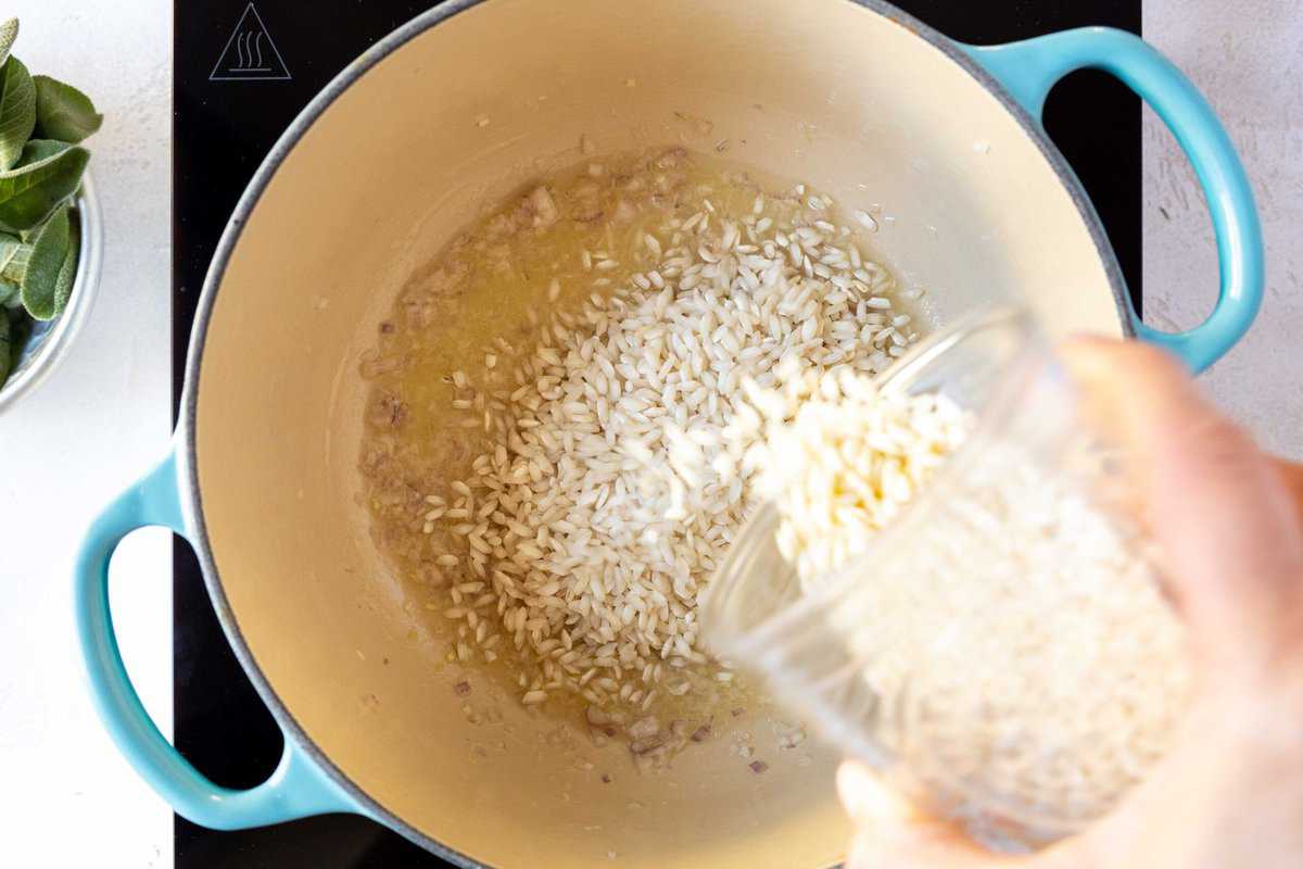 Rice being poured into a dutch oven pot with butter and chopped shallot to be toasted.