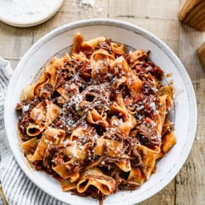 A white bowl filled with homemade Short Rib Ragu, sprinkled with fresh parmesan cheese.