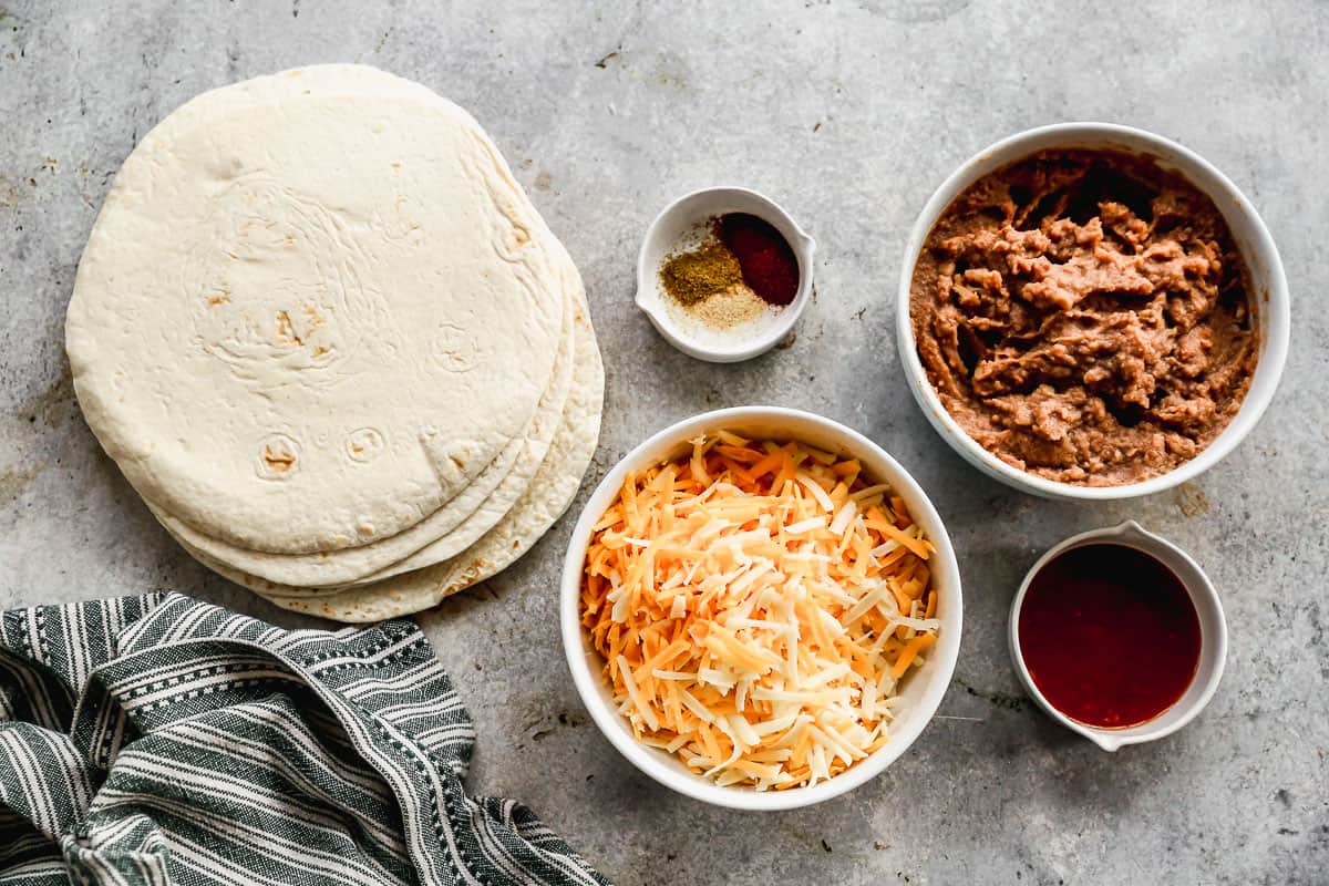All of the ingredients needed for Bean and Cheese Burritos: tortillas, refried beans, cheese, spices, and salsa.