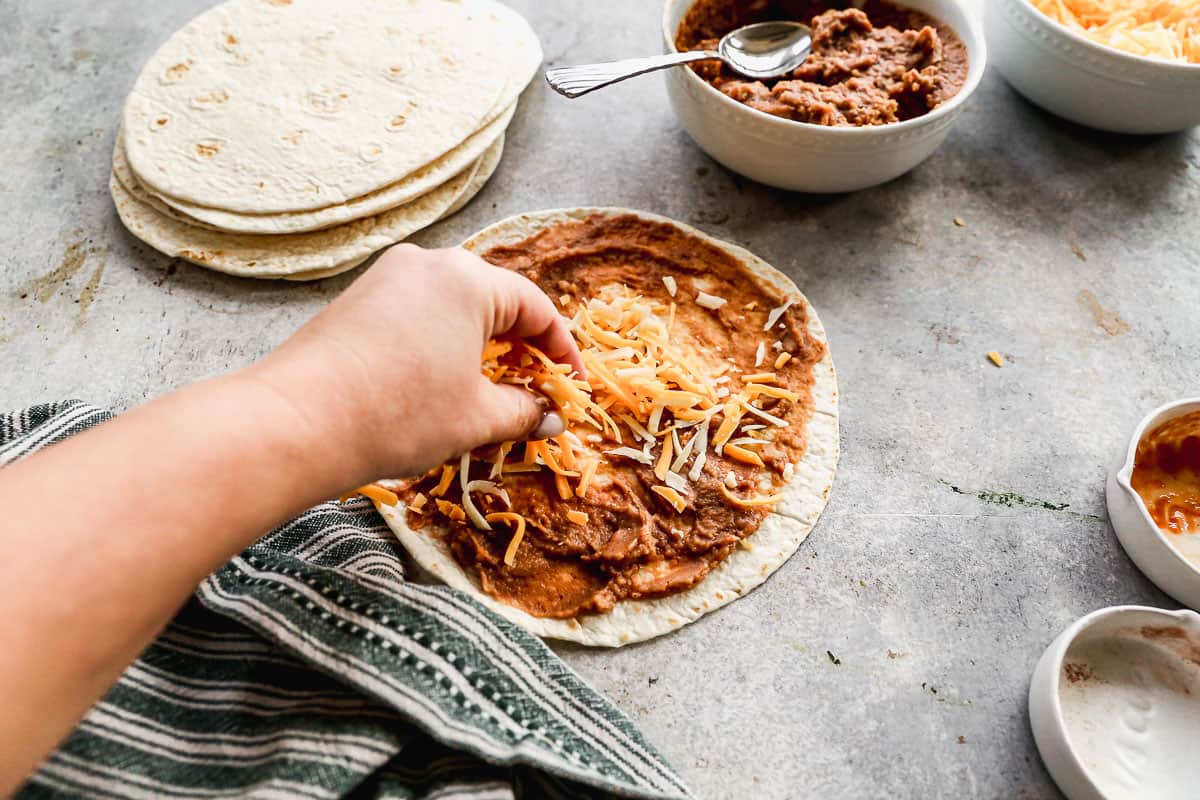 Campuran keju Meksiko yang disebarkan di atas tortilla dengan kacang di atasnya untuk membuat burrito kacang dan keju yang renyah.